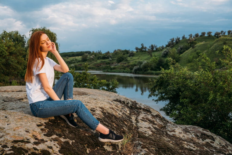 Woman meditating outdoors in nature for mental wellbeing and relaxation.