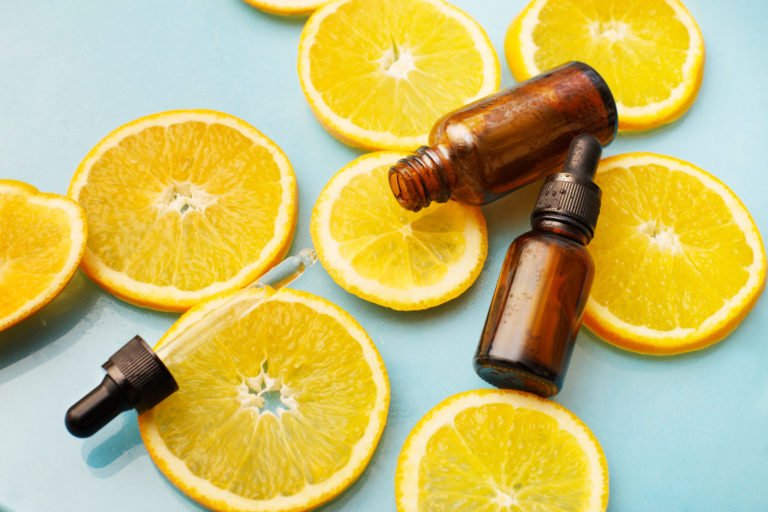Brown glass bottle with pipette and vitamin C serum surrounded by orange slices.