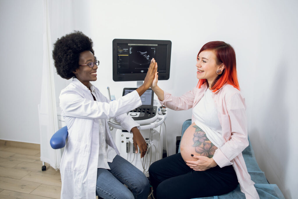 Pregnant woman and midwife celebrating with high-five during ultrasound appointment