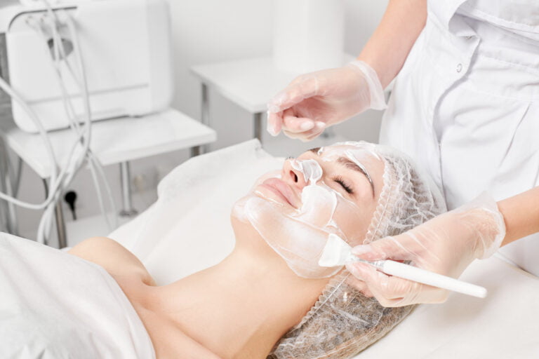 Beautician applying cream mask on woman's face for rejuvenation and cosmetic procedures.