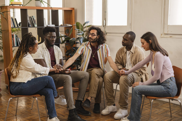 Group therapy session with people holding hands, addiction recovery support.